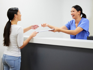 Smiling dental assistant handing patient form