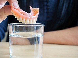 Man dropping his dentures in a cleaning solution